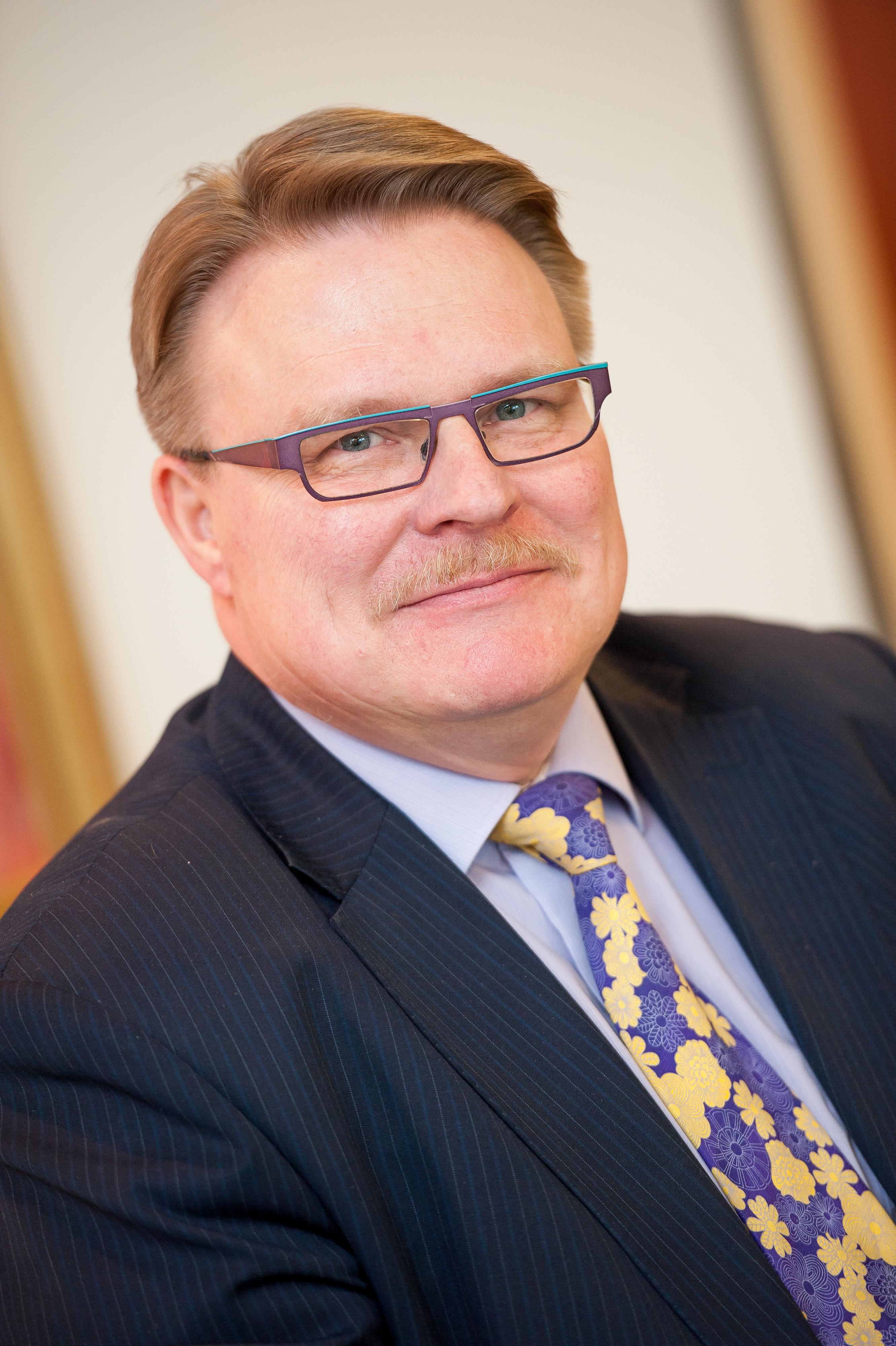 Invalidiliiton pääjohtaja Petri Pohjonen. Hänellä on vaaleanruskeat hiukset, silmälasit, tumma puvuntakki, vaaleansininen paita ja sini-keltainen solmio.