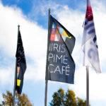 Lippuja liehumassa ulkona, yhdessä lukee: "Iiris Pimé Café"