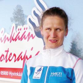 Päivi Tolppasella on vaaleat kiharat hiukset poninhännällä ja sinivalkoinen Finland-verryttelytakki.