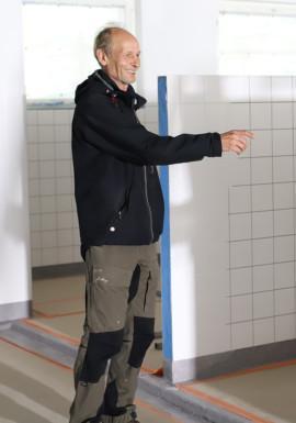 Mies seisoo keskeneräisen opaskoirakoulun sisällä ja osoittaa hymyillen sormellaan oikealle.