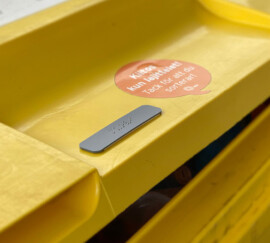 Keltaisessa roskalaatikossa pistekirjoituslaatta. Vieressä puhekuplan mallinen tarra, jossa lukee "Kiitos kun lajittelet! Tack för att du sorterar!""